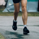 Runner wearing black Mount to Coast R1 running shoes, in motion during a run on a paved surface. #Color_black