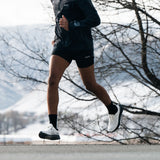 Runner wearing S1 white running shoes, demonstrating performance footwear for road and trail. #Color_white|black